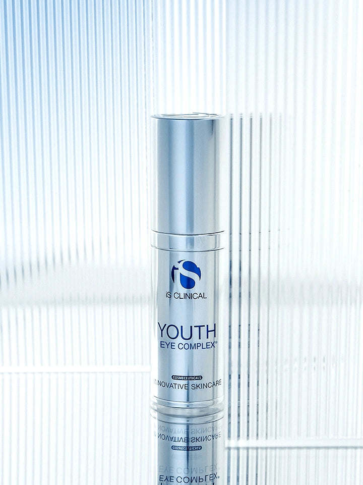 iS Clinical Youth Eye Complex silver bottle on reflective glass background for hydrating under eye treatment and care daily.