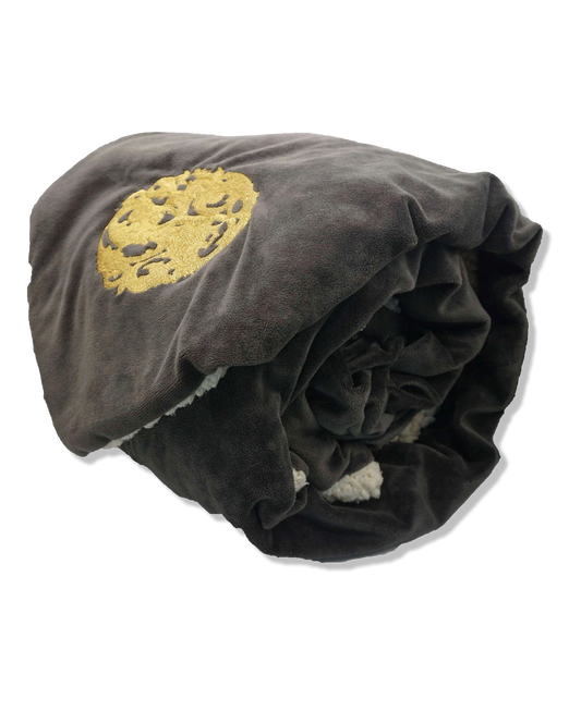 Nazarian swag sherpa fleece blanket rolled with dark plush exterior, ivory lining, and gold embroidered logo detail.