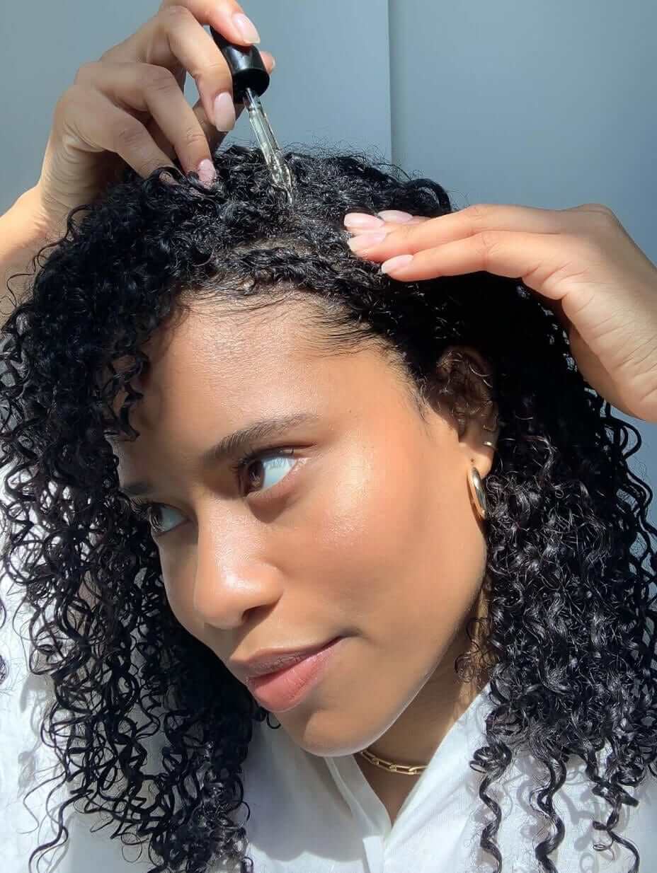 Nutrafol Women's Hair Growth Serum applied by dropper to curly scalp to hydrate, nourish, and support thicker hair growth...