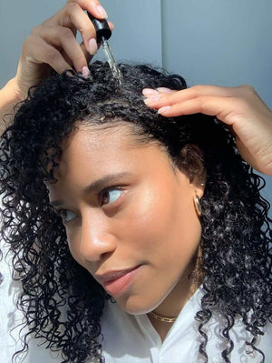 Nutrafol Women's Hair Growth Serum applied by dropper to curly scalp to hydrate, nourish, and support thicker hair growth...