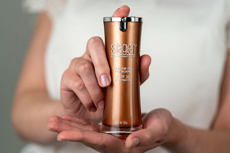 Person holding Silagen silicone scar gel with SPF 30 (30g) bottle, showing pump packaging for daily scar protection.