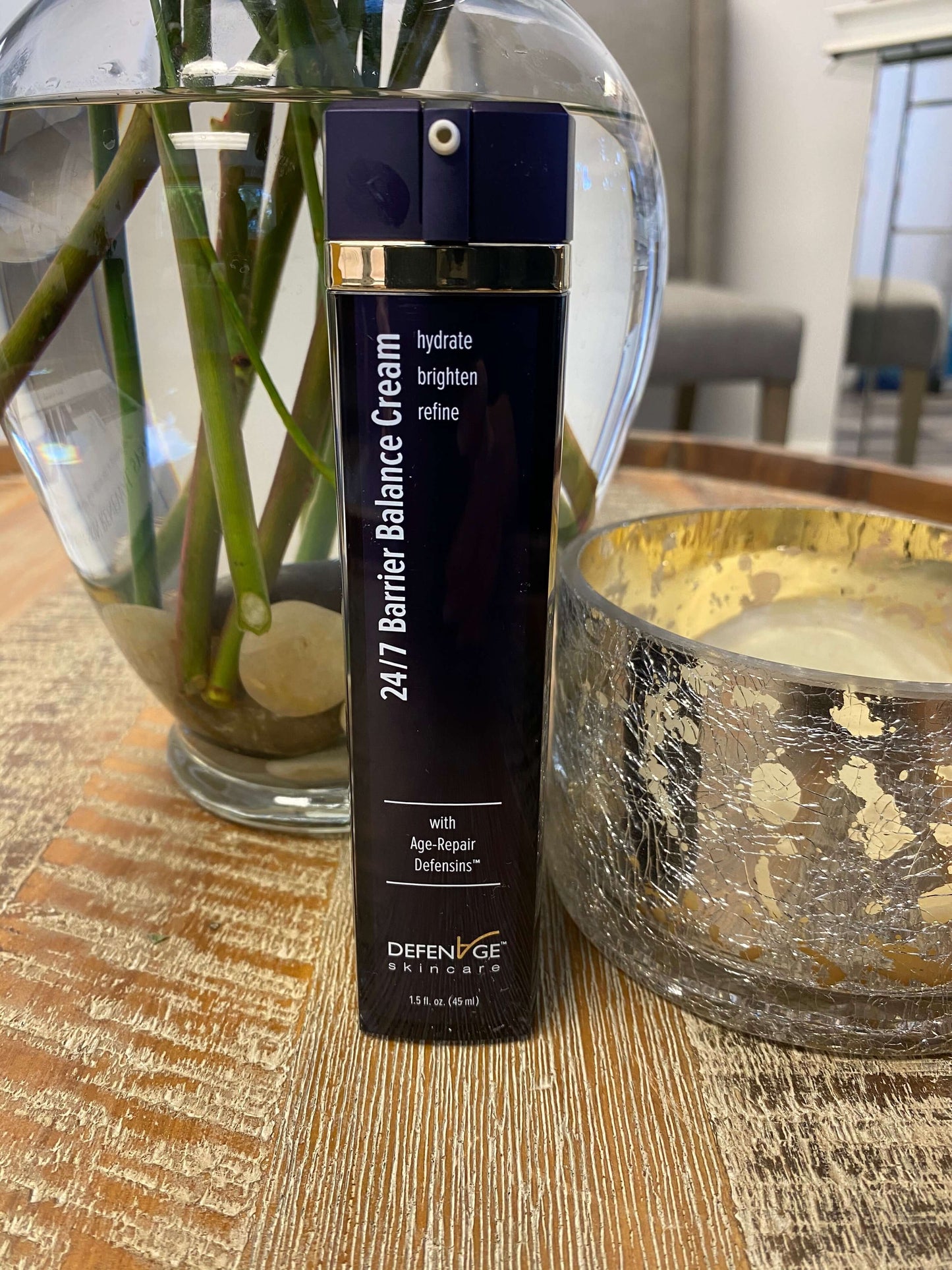 DefenAge 24/7 Barrier Balance Cream lifestyle bottle beside vase and candle shows hydrate, brighten and refine face care use