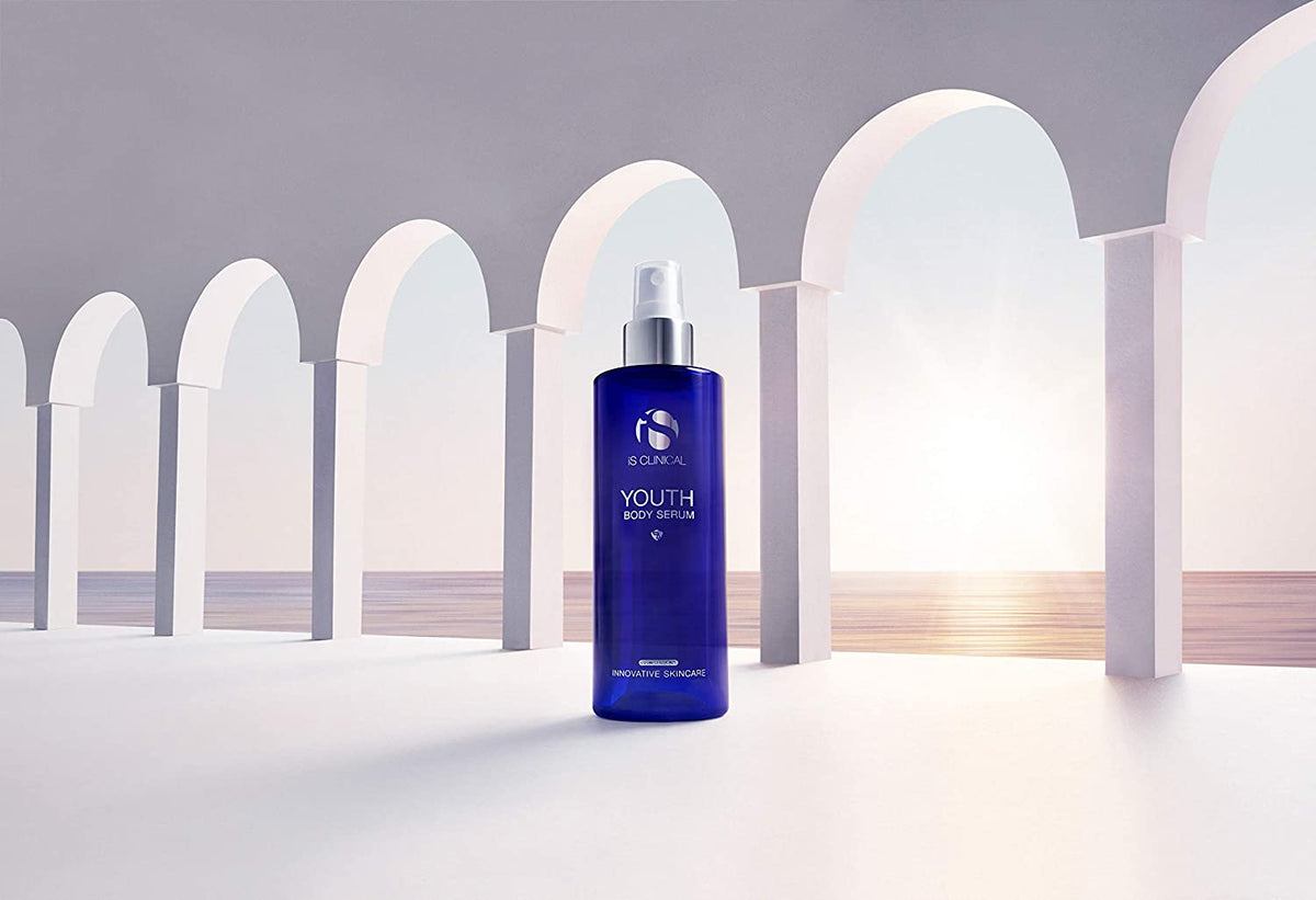 iS Clinical Youth Body Serum bottle in archway scene near sunset for antioxidant body care and post-sun skin hydration uses.