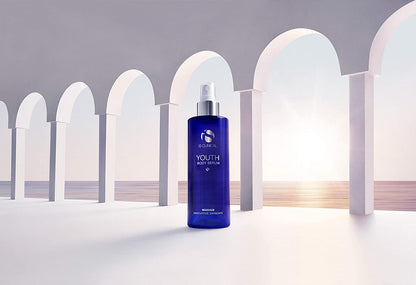 iS Clinical Youth Body Serum bottle in archway scene near sunset for antioxidant body care and post-sun skin hydration uses.