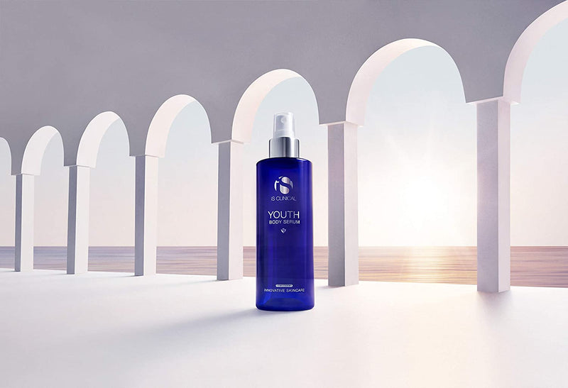 iS Clinical Youth Body Serum bottle in archway scene near sunset for antioxidant body care and post-sun skin hydration uses.