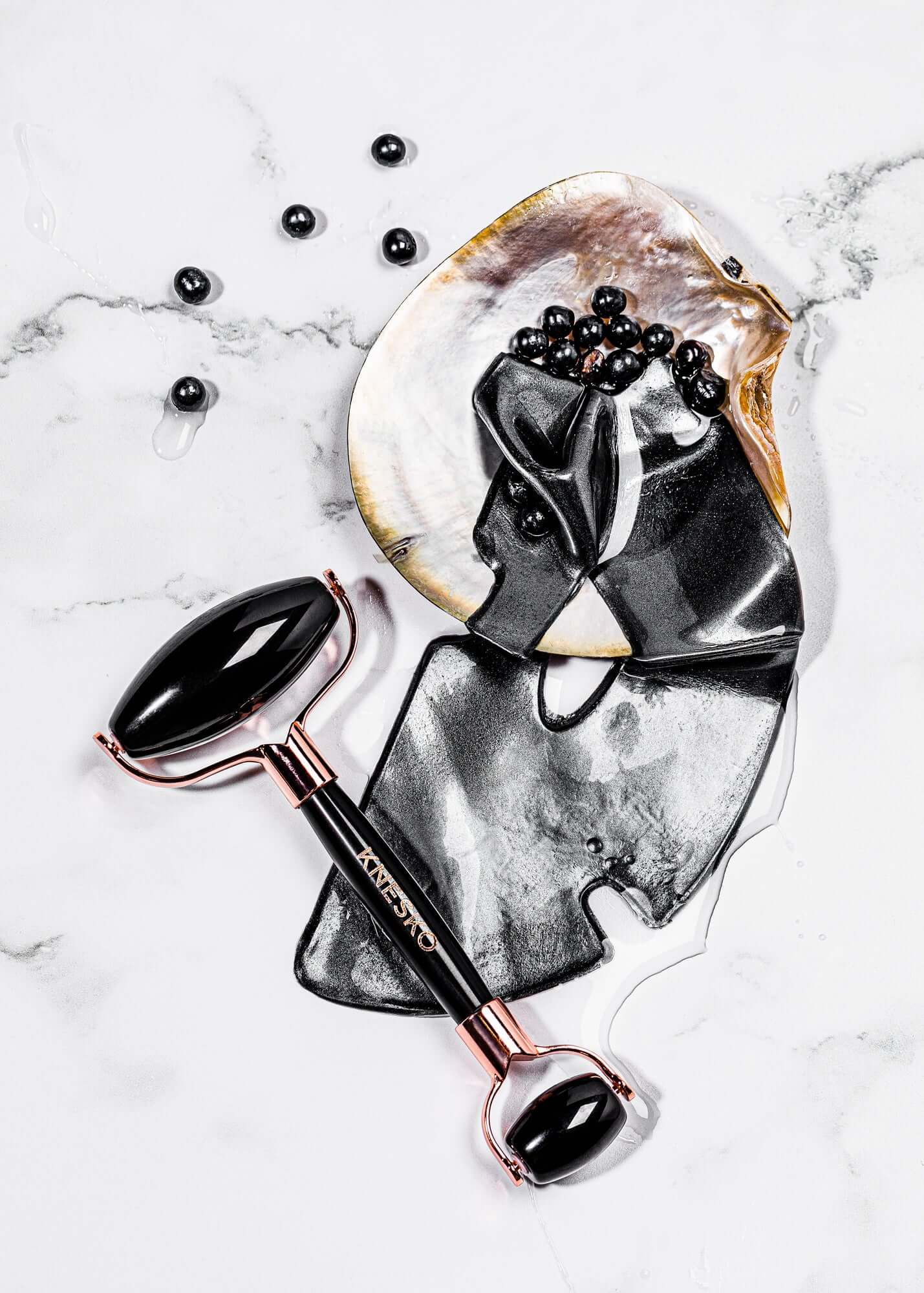 Knesko black collagen face mask and black gemstone facial roller styled on marble with serum and pearl details displayed now