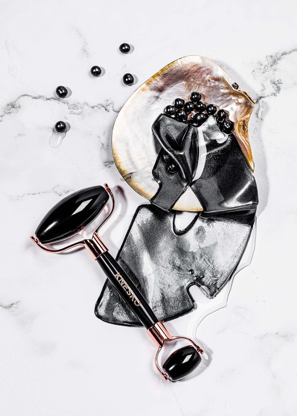 Knesko black collagen face mask and black gemstone facial roller styled on marble with serum and pearl details displayed now