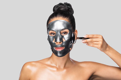 Model wearing black Knesko face mask while rolling cheek with dual-ended skincare tool for a lifted look during home spa use