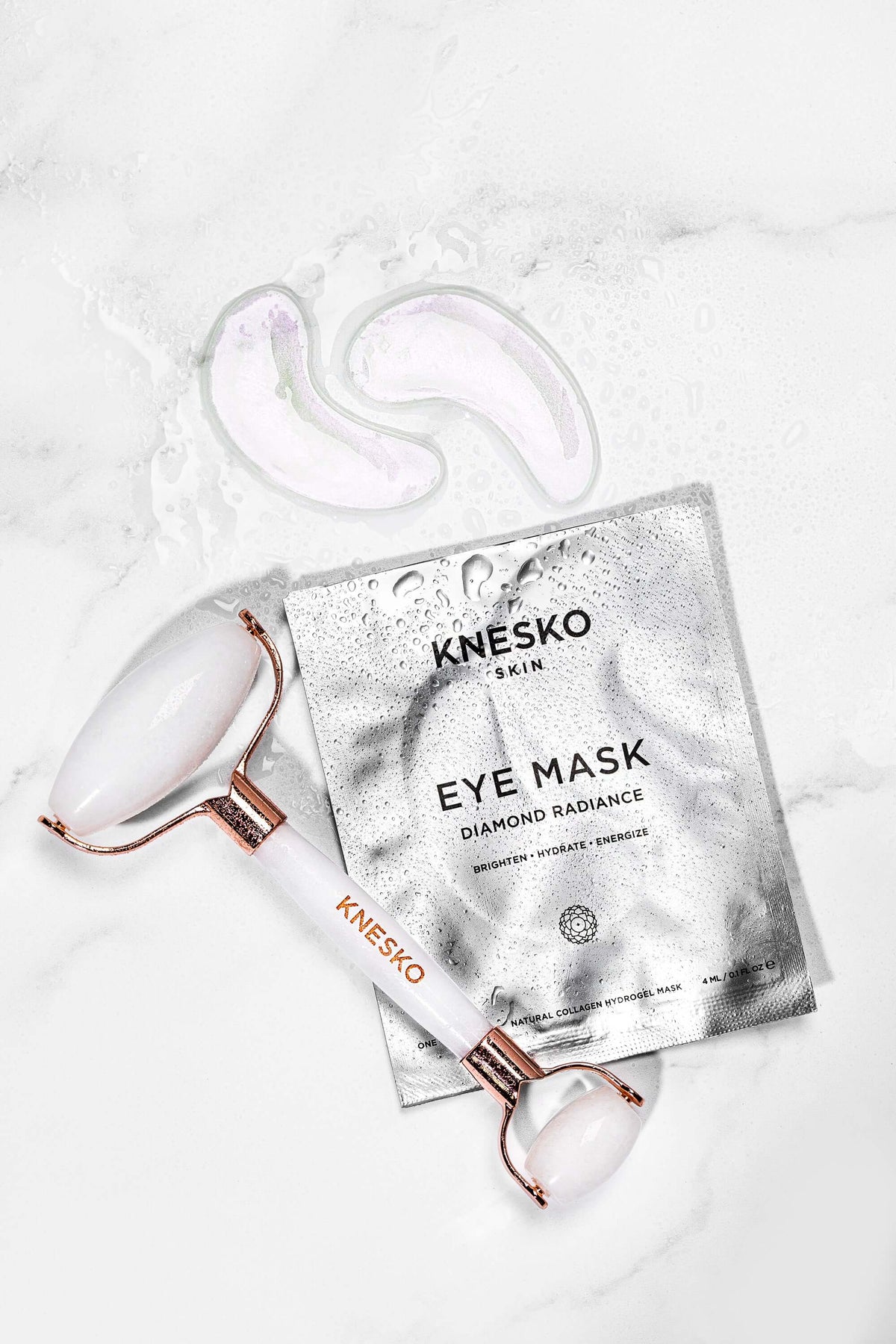Knesko Diamond Radiance Eye Mask pouch with white facial roller and eye masks styled on wet marble surface for travel care..