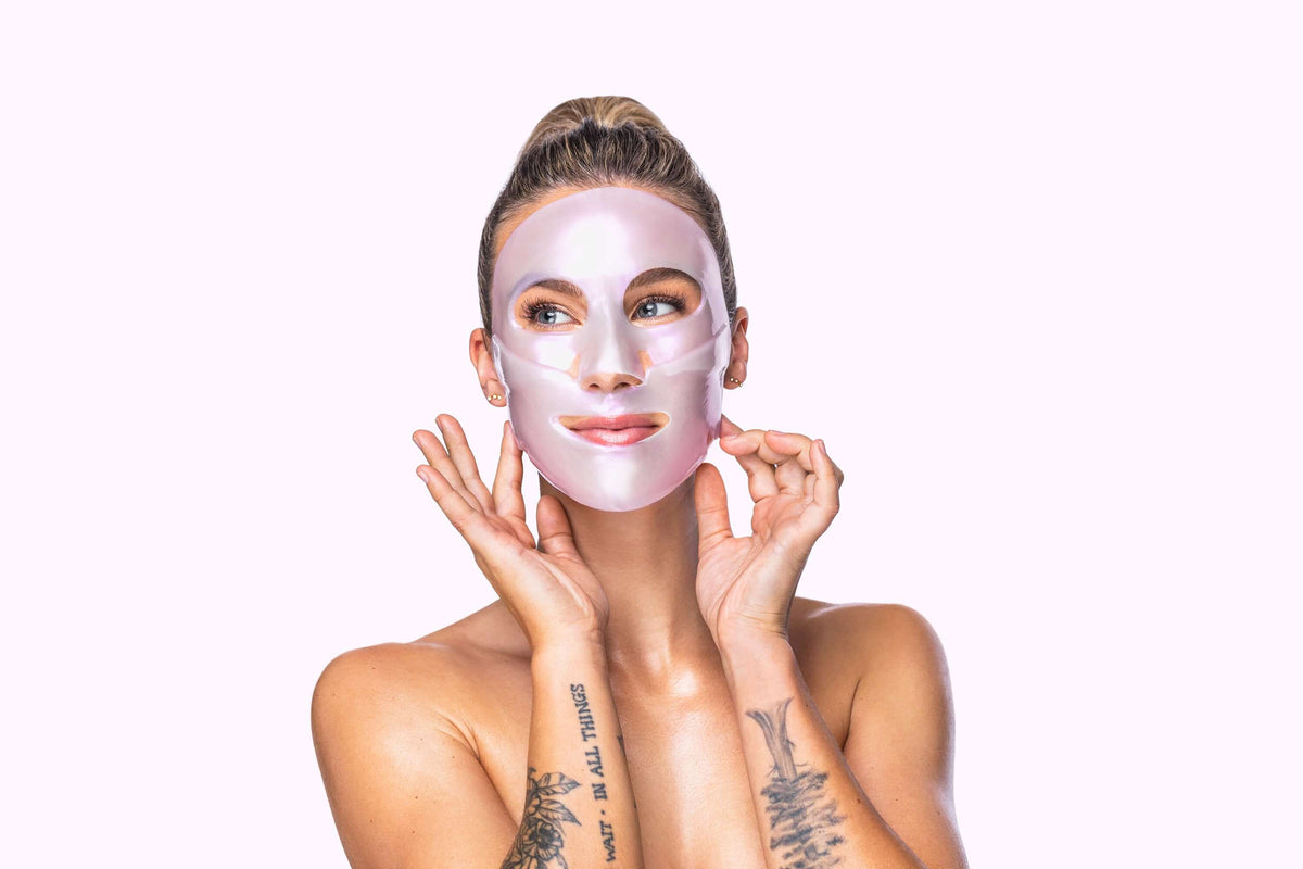 Model wearing pink Knesko collagen face mask for a luxury travel skincare ritual to brighten and hydrate skin at home today.
