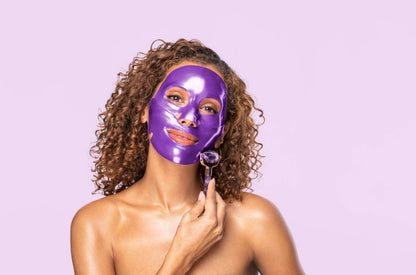 Model wearing purple Knesko collagen face mask while using facial roller for a bright hydrating skincare ritual at home use.