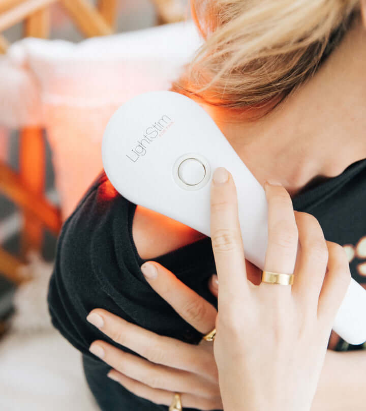 LightStim for Pain device used on shoulder with red LED light to target neck tension, soreness, and muscle aches at home use