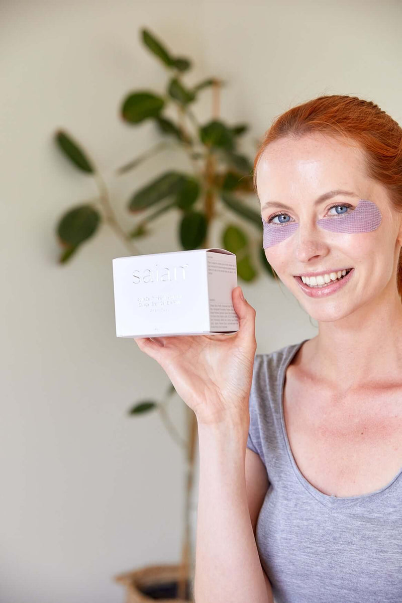 Saian ActiveCell Collagen Stem Cell Eye Pads model holds box while wearing purple under-eye patches for spa care.